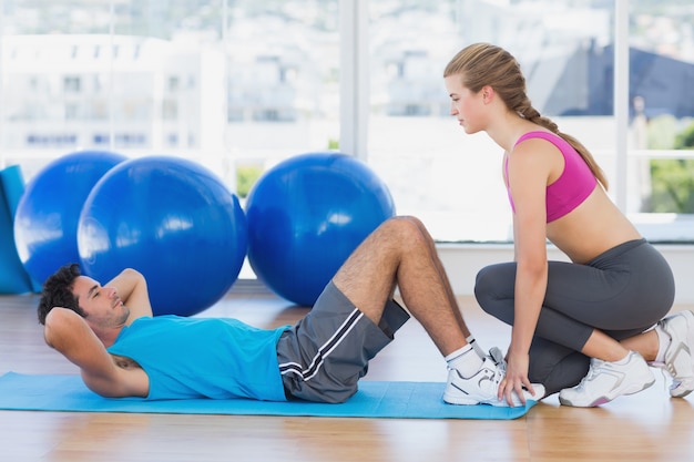 Entraîneur féminin aidant l&#39;homme avec ses exercices au gymnase