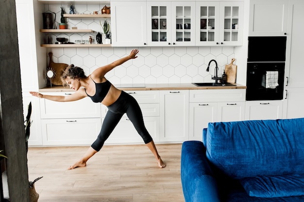 Entraîneur de fitness fille sportive montre des leçons en ligne Jeune fille bouclée en bonne santé faisant du yoga à la maison tout en