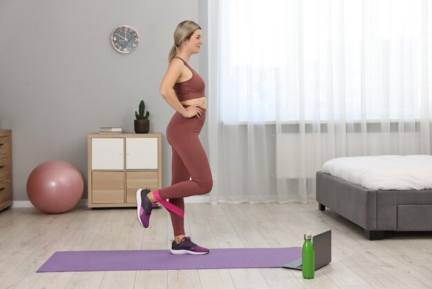 Entraîneur de fitness en ligne Femme faisant de l'exercice avec une bande élastique près de l'ordinateur portable à la maison