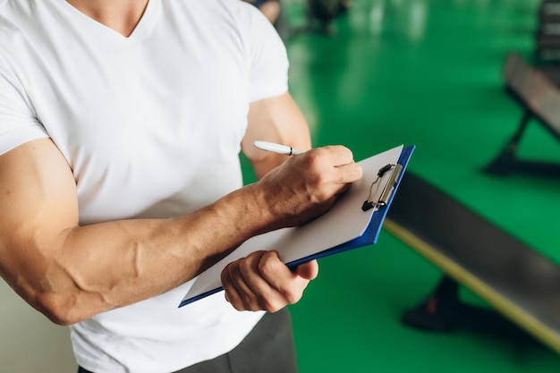 Entraîneur de fitness personnel avec plan d'entraînement en gros plan dans le fond de la salle de sport Fitness sportif et concept de style de vie sain