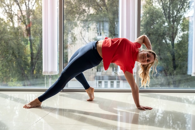 L'entraîneur de fitness pratique le yoga pour un dos en bonne santé près des fenêtres de la salle de sport