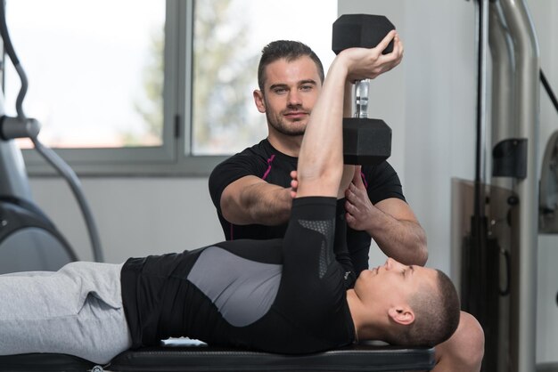 Entraîneur de gym aidant l'homme à faire de l'exercice sur la poitrine