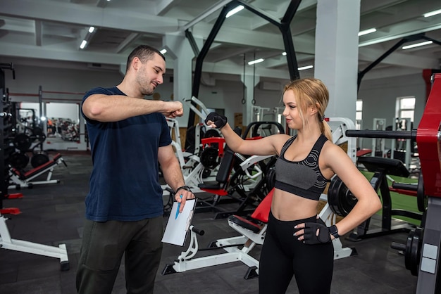 L'entraîneur de l'homme aide sa cliente mince à faire de l'exercice avec des haltères lourds au gymnase Concept de remise en forme et de gym pour la santé