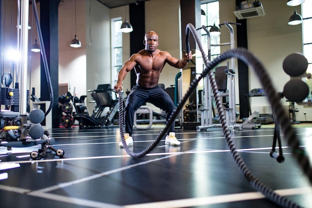 Entraîneur mulâtre soulevant des poids sur fond sombre dans une nouvelle salle de sport