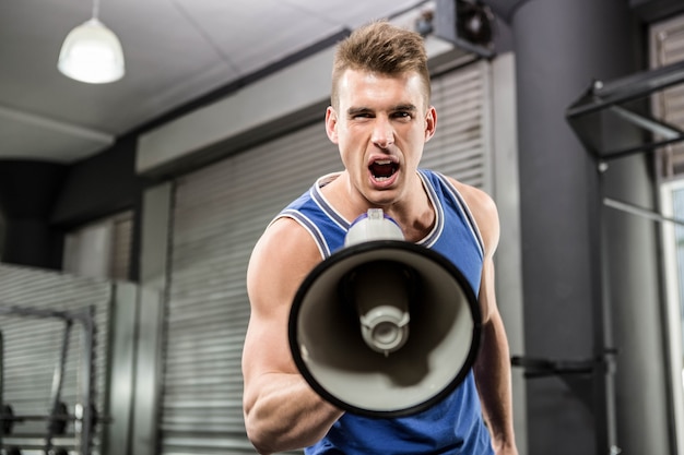 Entraîneur musclé criant sur un mégaphone à la salle de gym crossfit