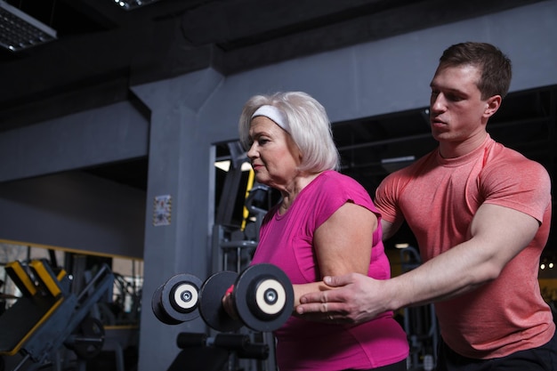 Entraîneur personnel aidant un client senior à faire de l'exercice avec des haltères