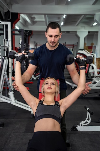 Entraîneur personnel avec une cliente mince faisant des boucles de biceps travaillant dans un mode de vie sain de gym