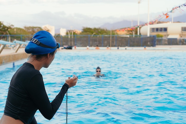 L'entraîneur personnel enregistre le temps sur le chronomètre au bord de la piscine pendant l'entraînement sportif