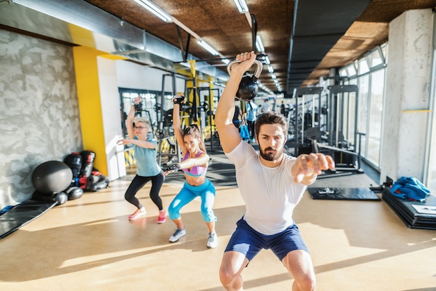 Entraîneur personnel montrant des exercices avec kettlebell à deux femmes sportives. Intérieur du gymnase.