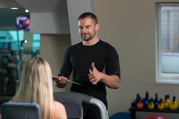 Entraîneur personnel montrant un signe OK au client Jeune femme exerçant les jambes sur la machine dans la salle de sport ou le club de remise en forme