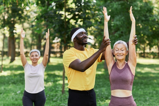 Entraîneur sportif souriant aidant une femme âgée active à faire de l'exercice en plein air