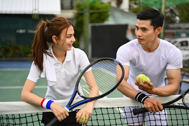 Entraîneur de tennis masculin expérimenté donnant des instructions à son élève debout près du filet sur le court de tennis extérieur