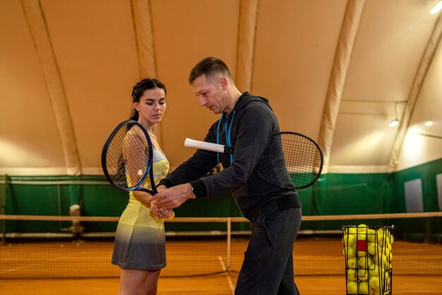 Un entraîneur de tennis masculin montre à une cliente comment servir sur le court