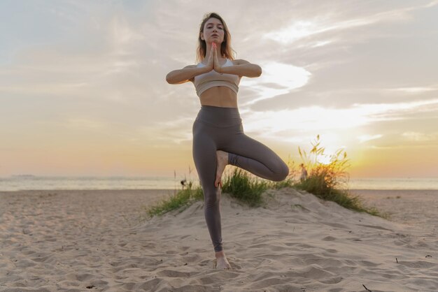 L'entraîneur de yoga féminin exerce une pose d'asana sur la plage en vêtements de sport
