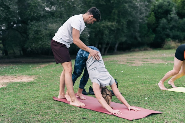 Entraîneur de yoga masculin corrigeant la posture du dos d'une femme qui fait du yoga dans un parc