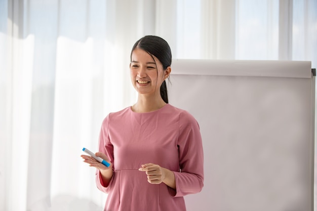 Une entraîneure ou une présentatrice souriante du millénaire discutent avec des collègues multiraciaux lors d'une réunion, une jeune tutrice heureuse fait une présentation sur un tableau blanc lors d'un briefing de bureau