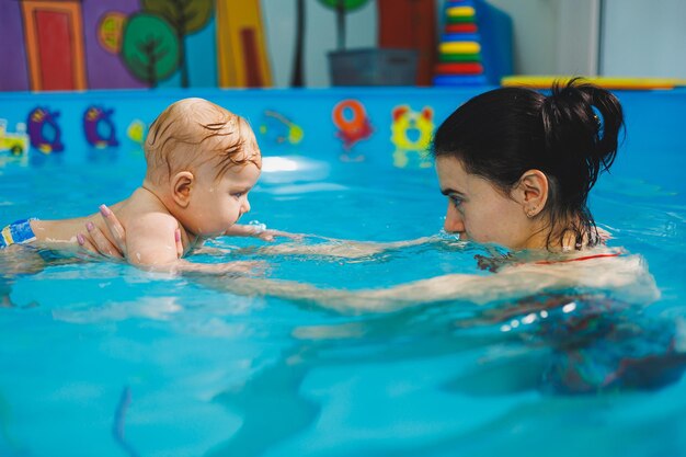 Une entraîneuse apprend à un bébé à nager dans la piscine et soutient ses mains Bébé nageant dans la piscine Apprendre à un nouveau-né à nager dans la piscine