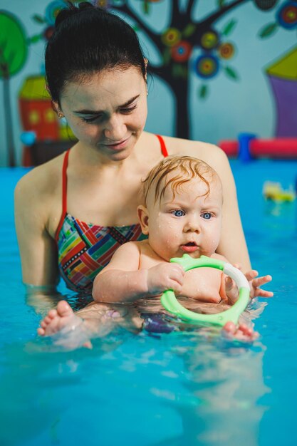 Une entraîneuse enseigne à un bébé à nager dans la piscine et soutient ses mains Bébé nageant dans la piscina Enseigne à un nouveau-né à nager Dans la piscine