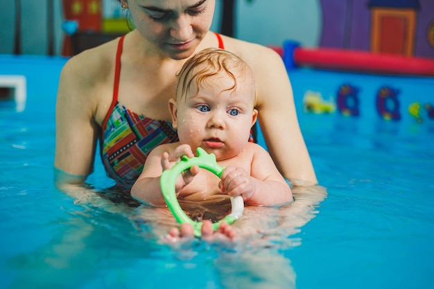 Photo une entraîneuse enseigne à un bébé à nager dans la piscine et soutient ses mains bébé nageant dans la piscina enseigne à un nouveau-né à nager dans la piscine