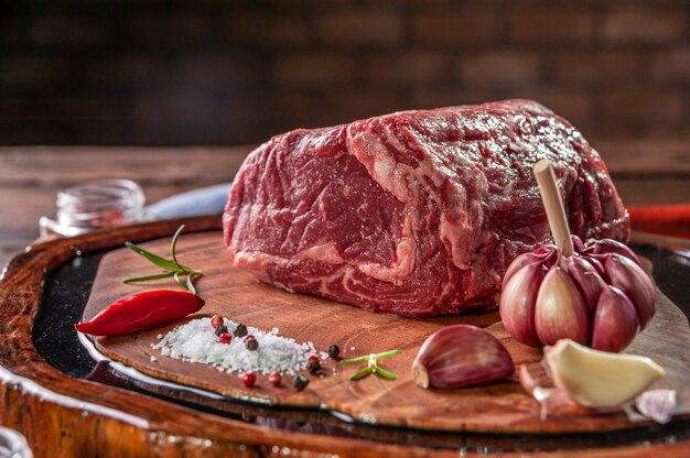 Entrecôte de boeuf crue sur une planche à découper en bois avec des épices sur fond de mur de briques - Gros plan.