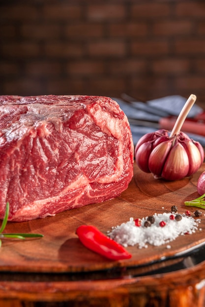 Entrecôte de boeuf crue sur une planche à découper en bois avec des épices sur fond de mur de briques - Gros plan.