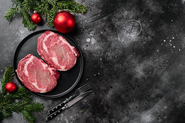 Entrecôte de bœuf crue avec poivre et herbes pour Noël et Nouvel An, sur fond de table en pierre noire foncée, vue de dessus à plat, avec espace de copie pour le texte