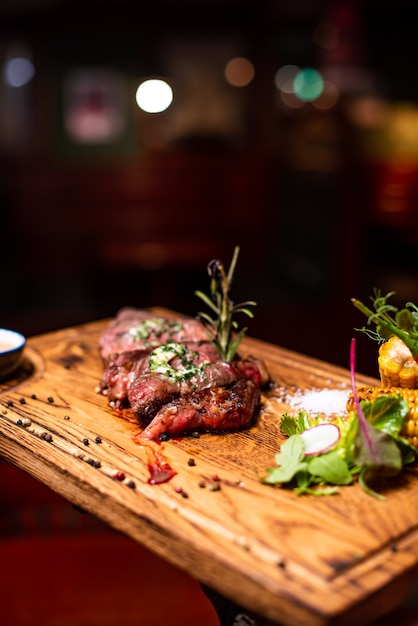 Entrecôte de boeuf Viande de steak grillée avec flammes de feu sur planche à découper en bois avec branche de romarin, poivre et sel. Chef cuisinier délicieux barbecue grill.