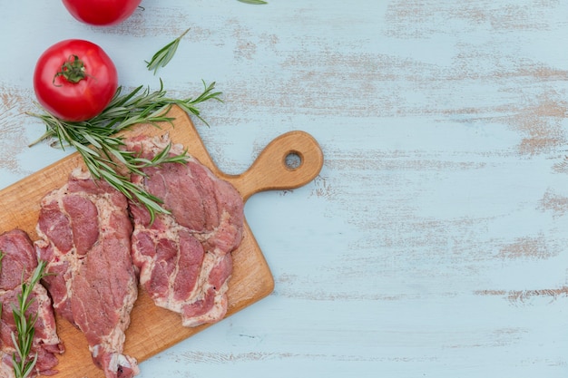 Entrecôte de steak de viande fraîche crue, tomates, romarin et assaisonnements sur planche à découper en bois