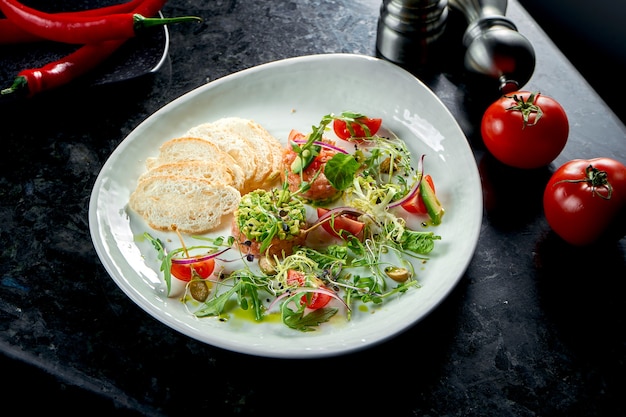 Une entrée française avant le plat principal - tartare de steak de saumon à l'avocat, tomates cerises et croûtons, servi dans une assiette blanche. Nourriture de restaurant. Vue d'en-haut