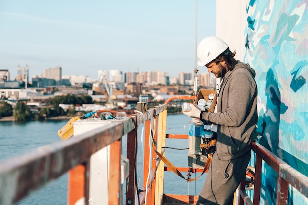 Entrepreneur, artiste à haute altitude dans un berceau de bâtiment effectue la peinture de façade, la décoration et la rénovation domiciliaire