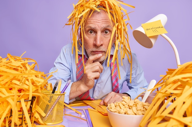 Photo un entrepreneur choqué pose sur le lieu de travail le budget a des céréales pour le petit-déjeuner porte une tenue formelle essaie de trouver l'âme pour le projet regarde émerveillé