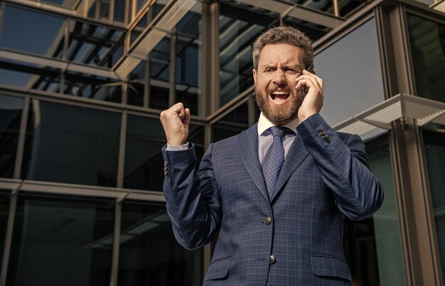 Entrepreneur en colère en costume criant pendant une conversation téléphonique à l'extérieur de la frustration du bureau