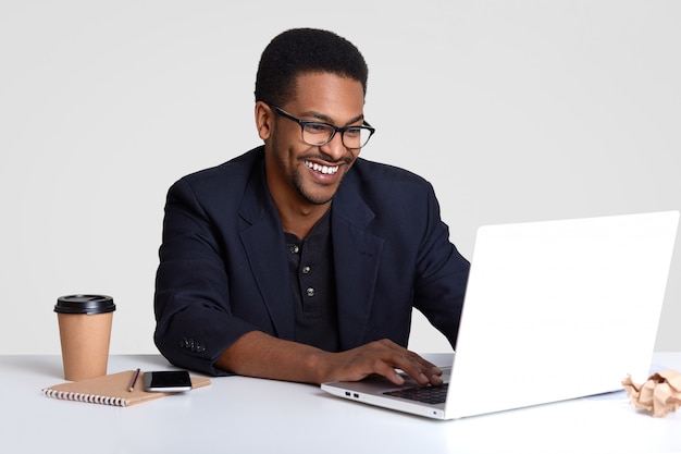 Entrepreneur homme souriant satisfait avec un sourire à pleines dents, porte des lunettes et un costume noir, des informations sur les claviers sur ordinateur portable