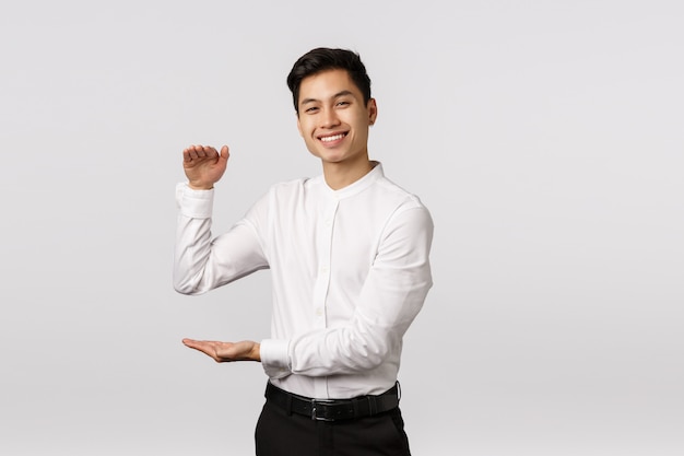 Entrepreneur masculin asiatique joyeux et beau, employé en chemise blanche, pantalon, montrant une grande boîte avec une expression heureuse, tenant le produit ou quelque chose de grand et satisfaisant