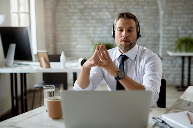 Entrepreneur masculin ayant une vidéoconférence sur un ordinateur portable tout en travaillant au bureau