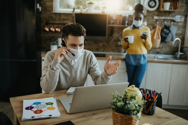 Entrepreneur masculin avec masque facial parlant lors d'une conférence téléphonique à la maison