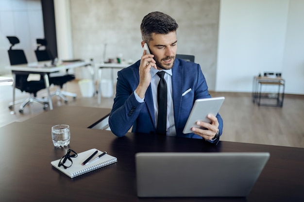 Entrepreneur occupé à parler au téléphone tout en utilisant le pavé tactile au bureau