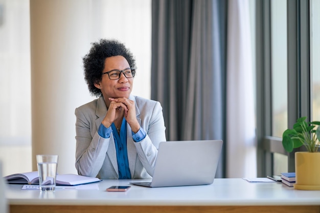 Entrepreneur réfléchi portant des lunettes regardant par la fenêtre au bureau