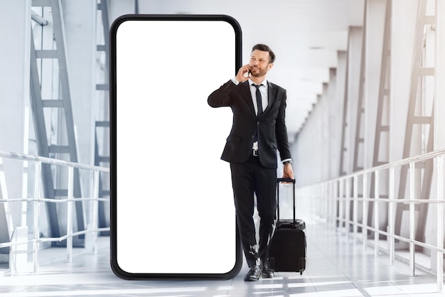 Entrepreneur riche avec une valise marchant près de l'aéroport ayant un appel téléphonique