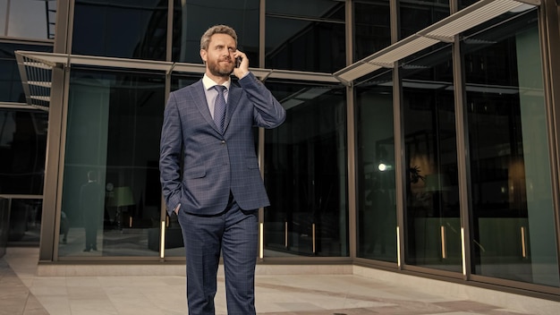 Un entrepreneur souriant en costume professionnel a une conversation téléphonique en dehors de l'appel d'affaires du bureau