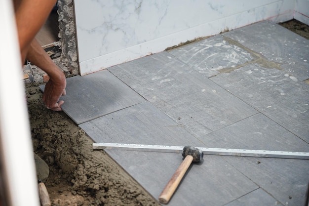 Entrepreneur travaillant avec un sol en carreaux de granit avec du ciment et des outils dans la salle de bain