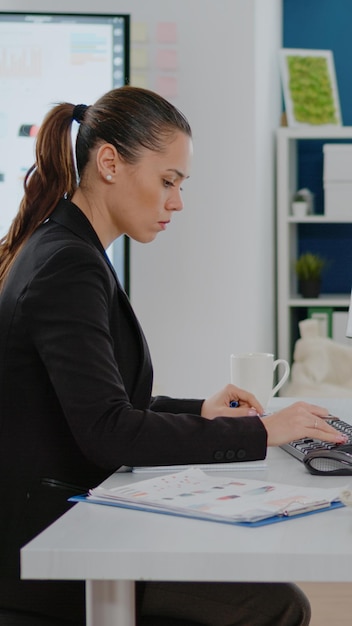 Entrepreneur utilisant un ordinateur pour travailler avec des tableaux de données sur papier et un moniteur au siège social. Femme d'affaires travaillant avec des idées pour la stratégie marketing et la planification de la gestion