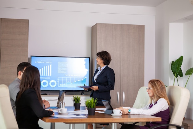 Des entrepreneurs et des hommes d'affaires prospères dans une salle de conférence analysant des graphiques et des diagrammes sur un téléviseur. Hommes d'affaires prospères