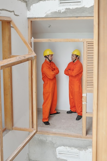 Entrepreneurs positifs debout à l'intérieur du bâtiment en construction et discutant du processus de rénovation