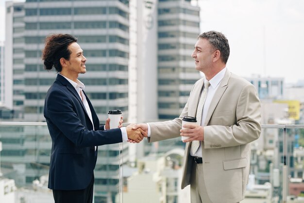 Des entrepreneurs souriants avec du café à emporter se serrant la main après une réunion réussie