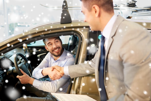 entreprise automobile, vente de voitures, consumérisme, concept de geste et de personnes - homme heureux avec un concessionnaire automobile faisant affaire et serrant la main dans un salon de l'auto ou un salon sur l'effet de neige