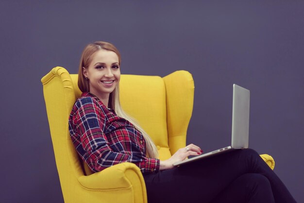 entreprise en démarrage, femme travaillant sur un ordinateur portable dans un bureau moderne et assise sur un fauteuil jaune créatif