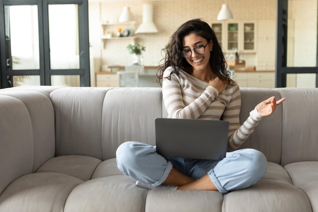 Entreprise à distance Jeune femme indépendante travaillant sur un ordinateur portable assis sur un canapé à la maison communiquant avec des collègues