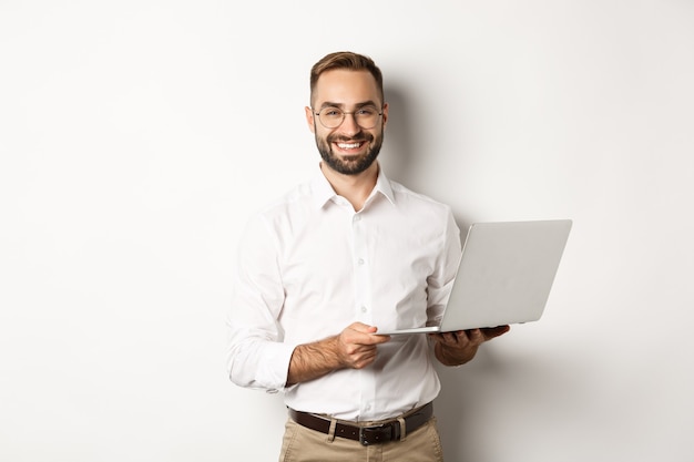 Entreprise. Homme d'affaires prospère travaillant avec un ordinateur portable, utilisant un ordinateur et souriant, debout sur fond blanc