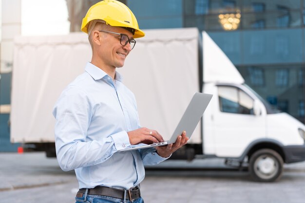 Entreprise. Ingénieur Travailleur Casque De Protection Utiliser Ordinateur Portable Contrôles Processus De Travail Inspecteur Superviseur Casque Jaune Lunettes Société De Transport Immeuble De Bureaux Et Fond De Camion